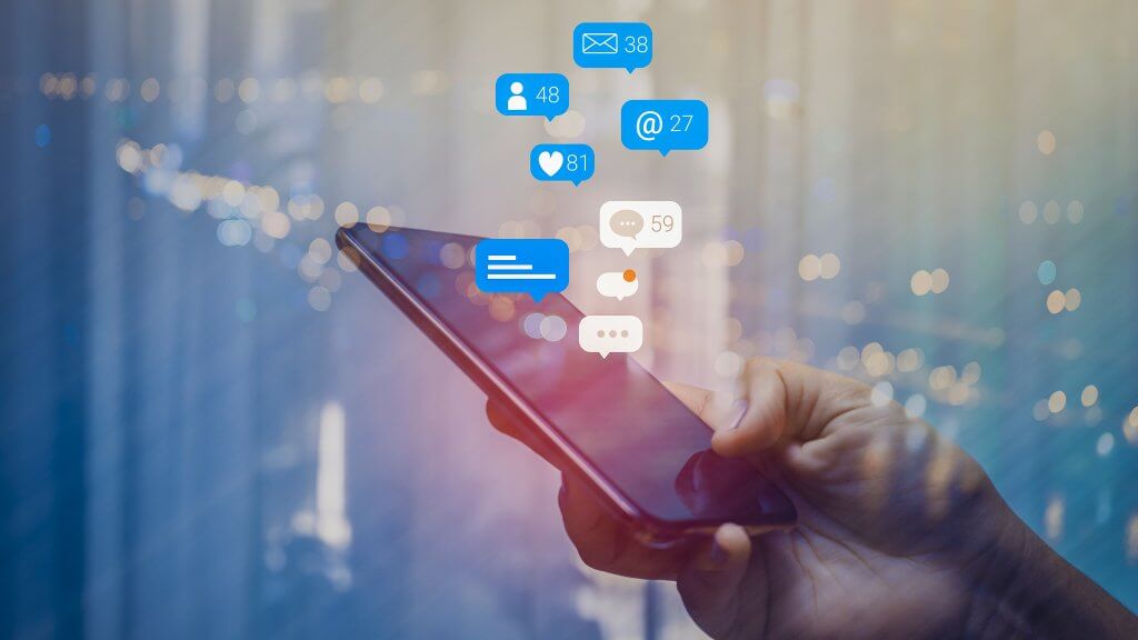 Person using a social media marketing concept on mobile phone with notification icons of like, message, comment and star above smartphone screen.